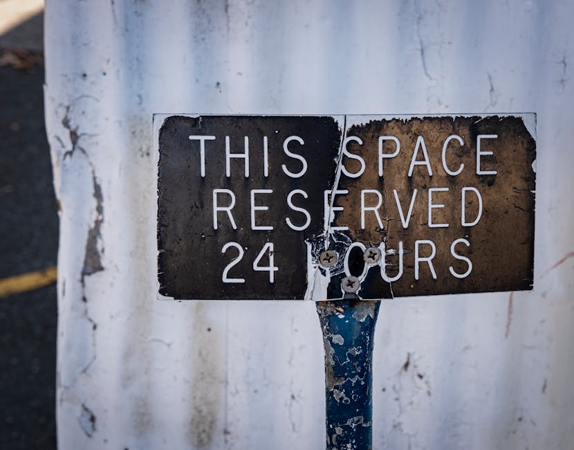 A white rectangular parking permit sign mounted on a wooden post in front of a red brick wall, featuring a blue wheelchair symbol at the top left corner indicating accessible parking, and a blue squar