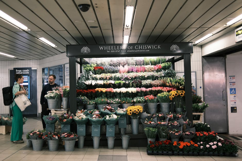 Inside a London underground station near Turnham Green Station, a flower stall operated by Wheeler of Chiswick displays a variety of colourful flowers and plants arranged in metal buckets and pots, in